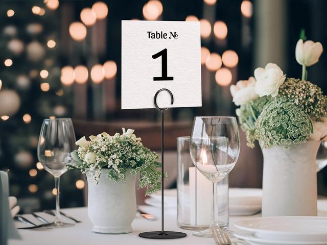 Elevate your event decor with this stylish table number display. Featuring a sleek holder and surrounded by elegant florals and candlelight, this setup adds a touch of sophistication to any wedding or formal gathering, ensuring a seamless and beautiful guest experience.