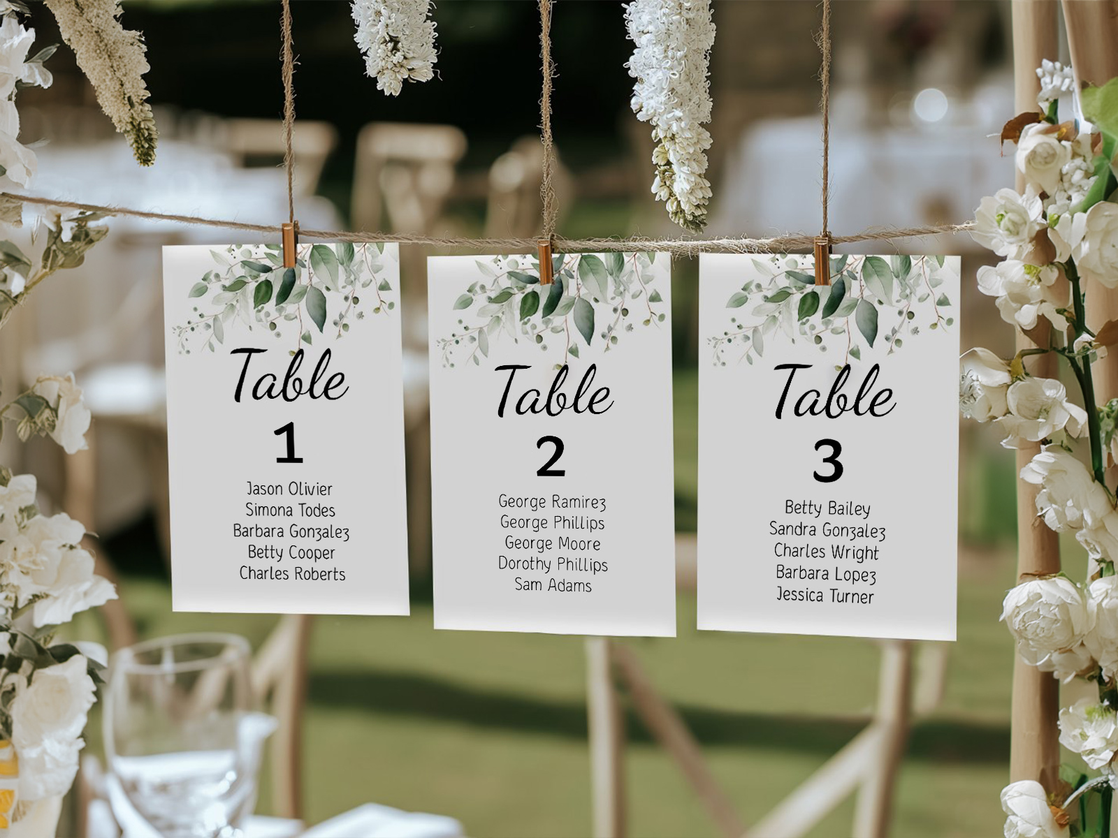 Trei carduri de așezare la mesele de nuntă cu antet verde acuarelă cu frunze, atârnate pe sfoară cu cleme din lemn, la o locație de nuntă în grădină, în aer liber