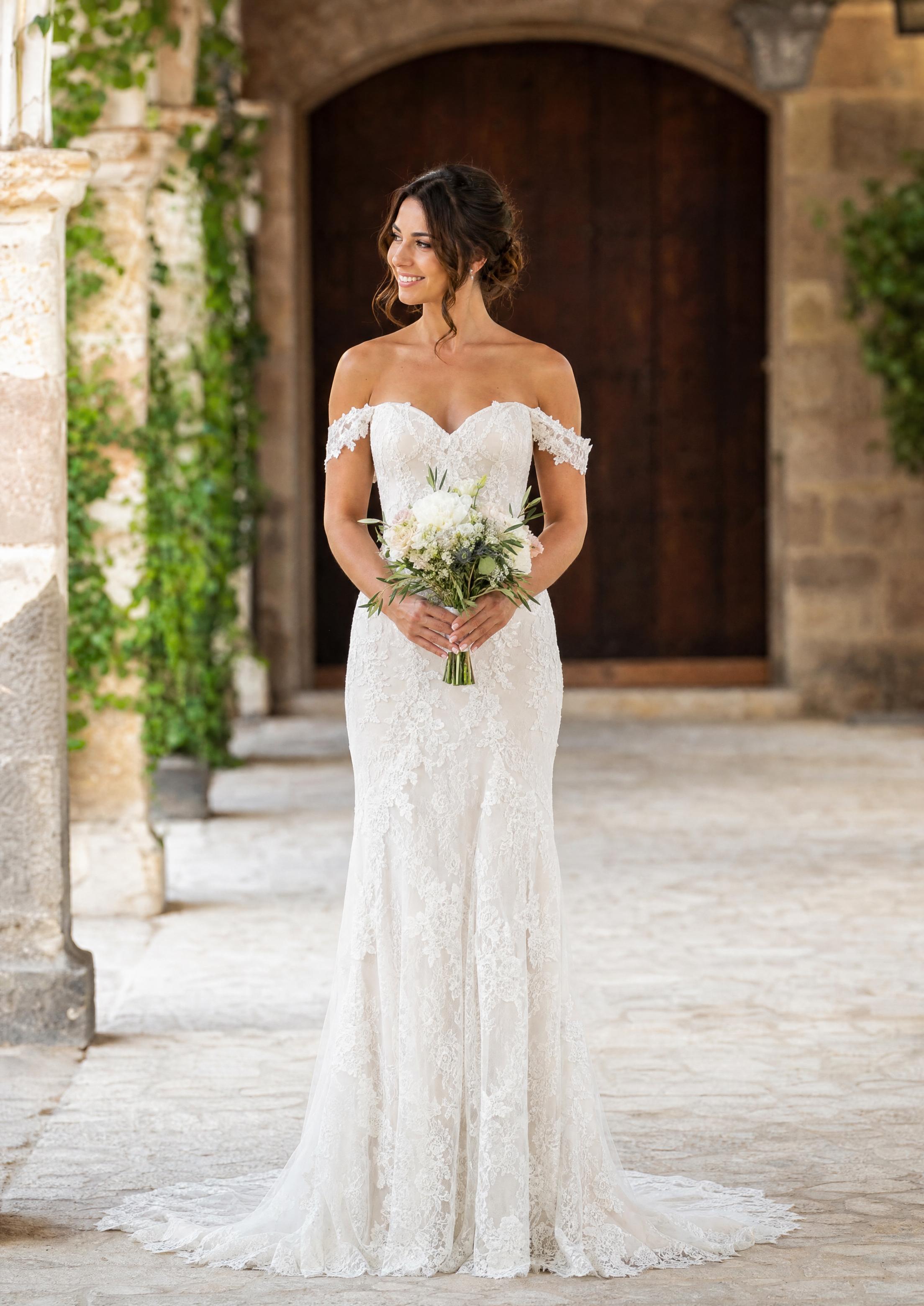 Núvia amb un vestit de núvia de punta d’espatlles caigudes amb mànigues curtes suaus que cauen sobre la part superior dels braços