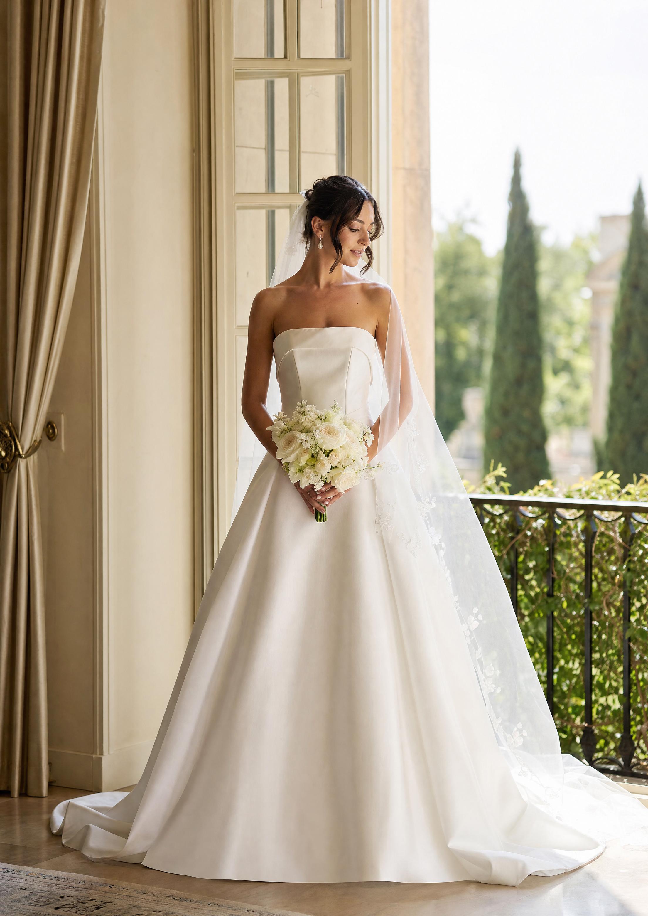 Núvia amb un vestit de núvia de setí estilitzat amb un vel suau i delicats pendents penjants de perla, refinada i elegant