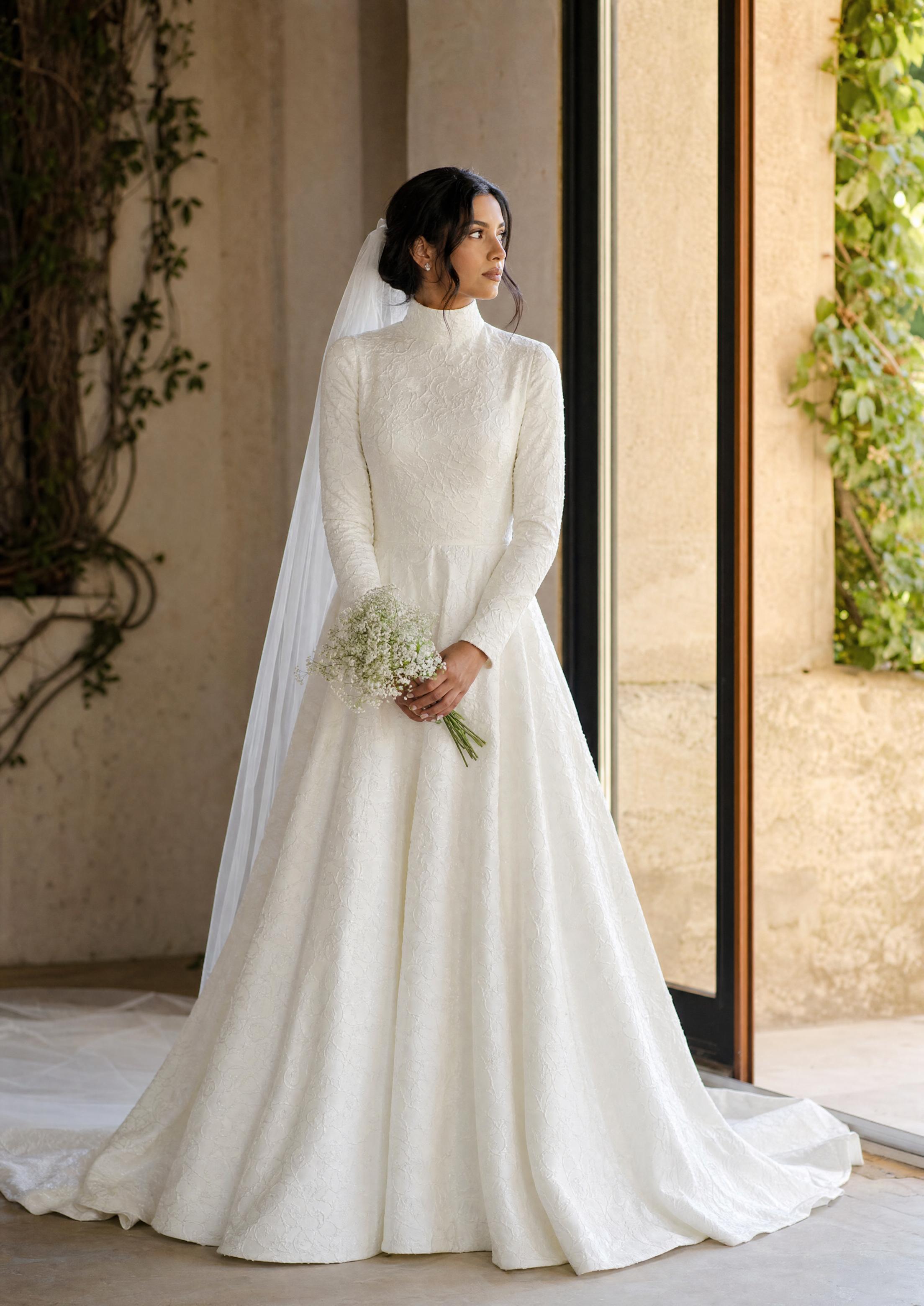 Núvia amb un elegant vestit de núvia discret de màniga llarga i coll alt, refinada i gràcil amb una llum natural suau