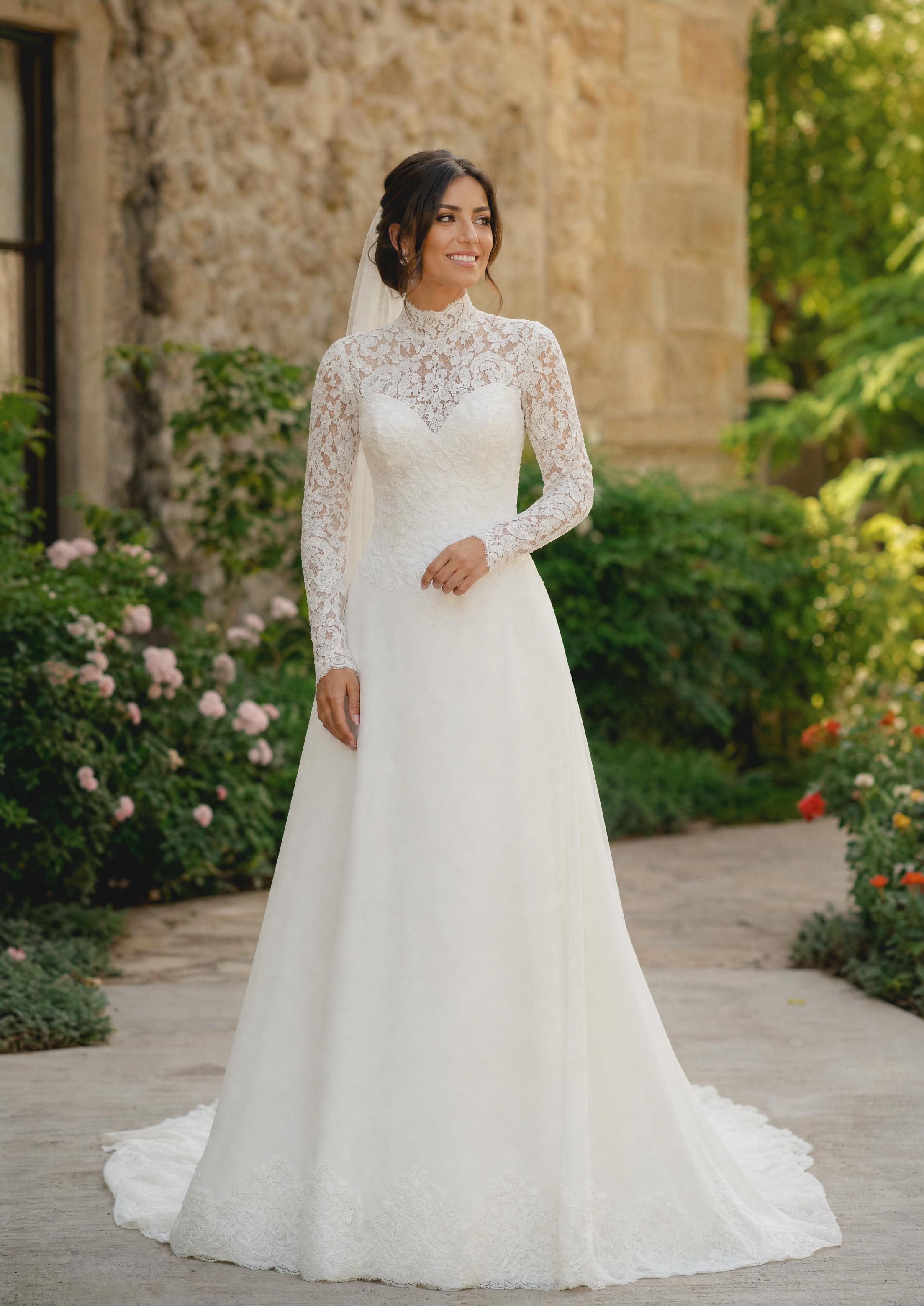 Núvia amb un vestit de núvia discret de línia A amb mànigues llargues de puntes i un escot alt, clàssic i afavoridor